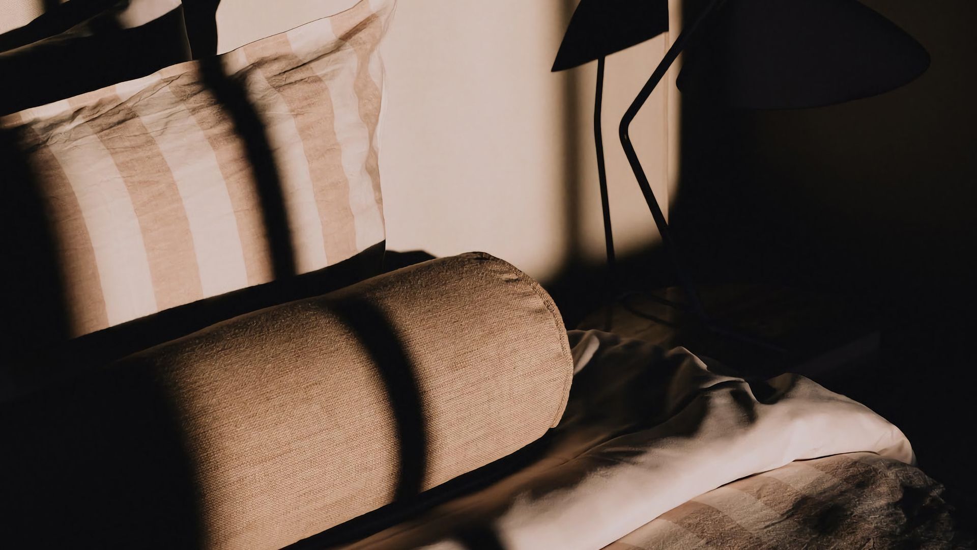 A close-up of a sofa with striped cushions and a dark floor lamp in a dimly lit room.
