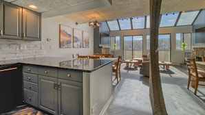 Une cuisine spacieuse dotée d’un grand îlot central, de meubles de couleur sombre et d’un pare-feu en marbre. On y trouve également un coin repas avec des meubles en bois et une grande fenêtre offrant une vue sur l’extérieur.