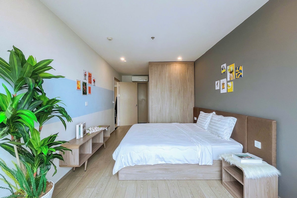Une chambre à coucher moderne avec un grand lit, une tête de lit en bois, une table de chevet, une plante en pot et une armoire.