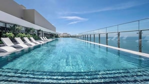 Een modern overloopzwembad met helderblauw water, omringd door ligbedden en glazen balustrades, met uitzicht op een schilderachtig zeegezicht.