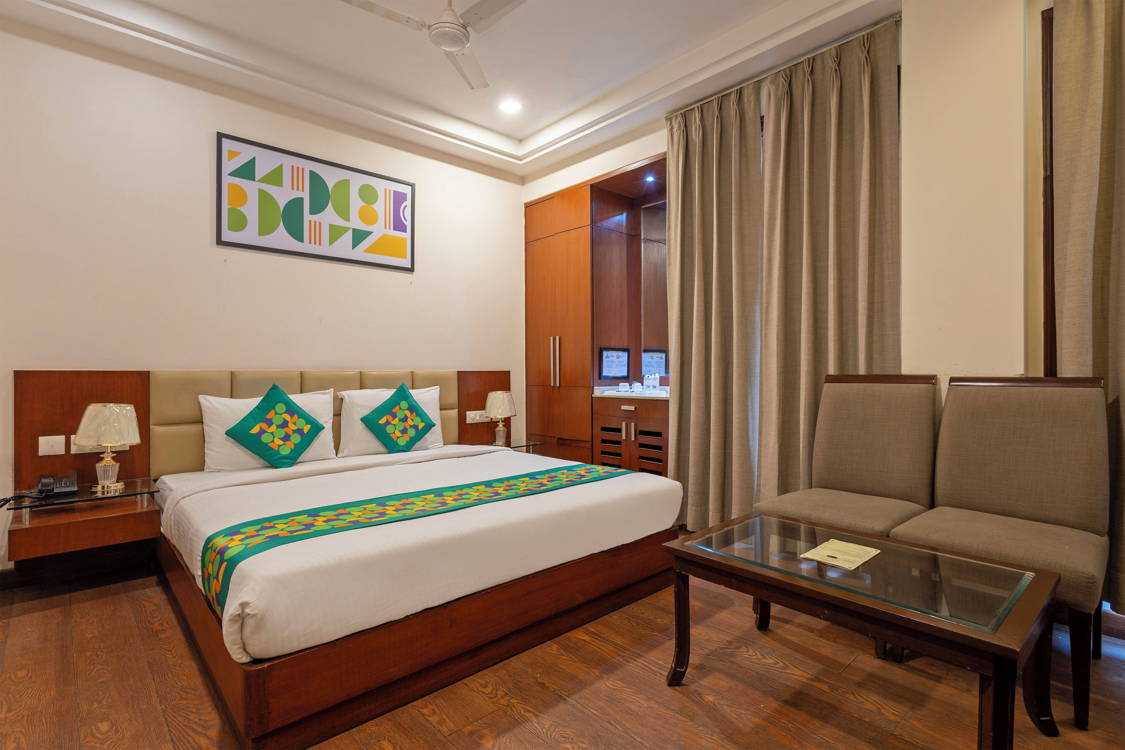 Quarto de hotel com cama, sofá, mesa de centro de vidro, escrivaninha com luminária e guarda-roupa.