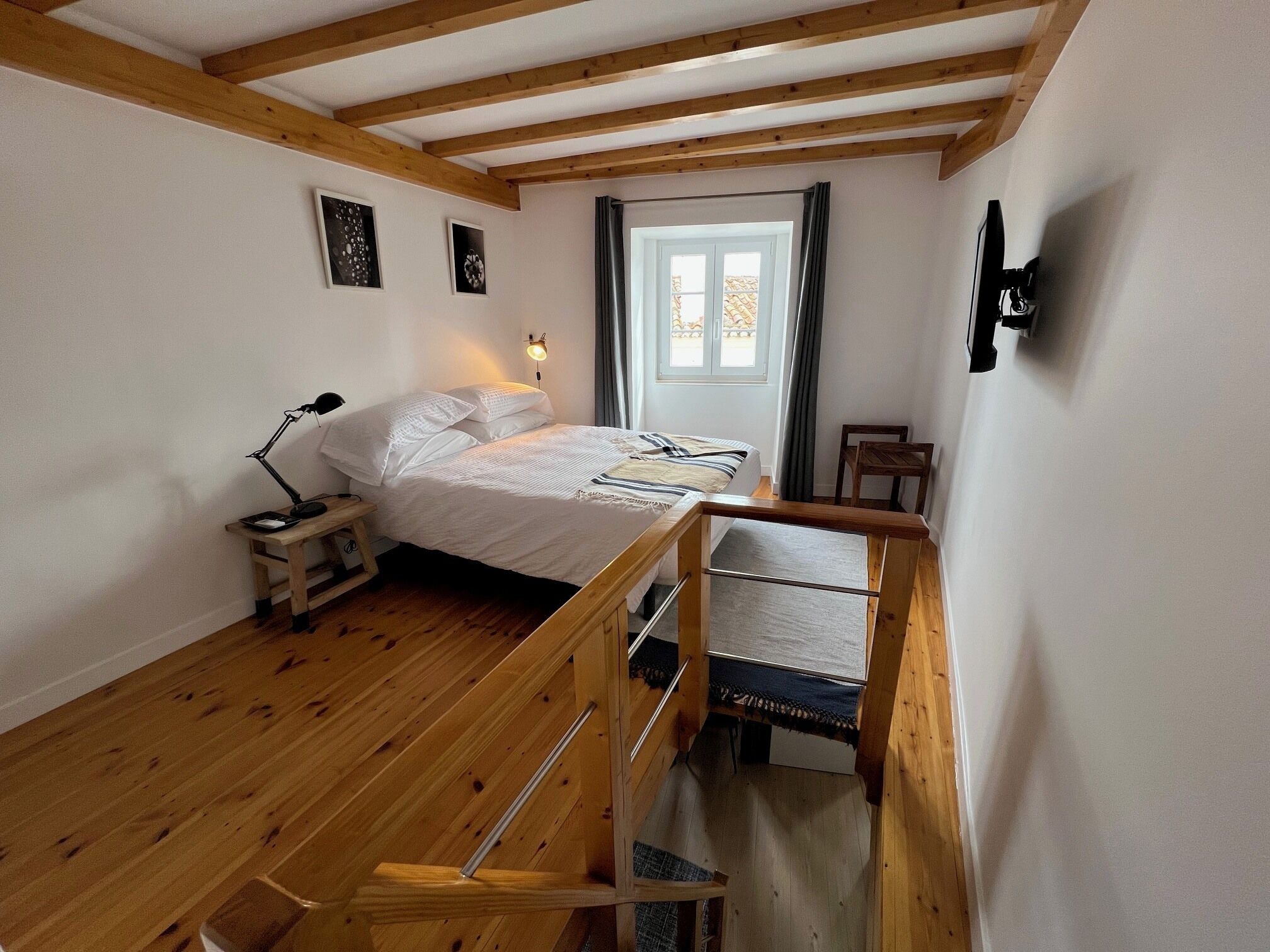 A bedroom with a wooden bed, a nightstand, a desk, and a window with curtains.
