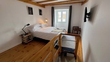 A bedroom with a wooden bed, a nightstand, a desk, and a window with curtains.