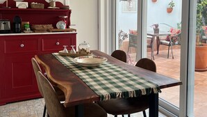 A kitchen with a red cabinet, a wooden dining table with chairs, and a view of the patio through large windows. - Constância Guest House (Constância)