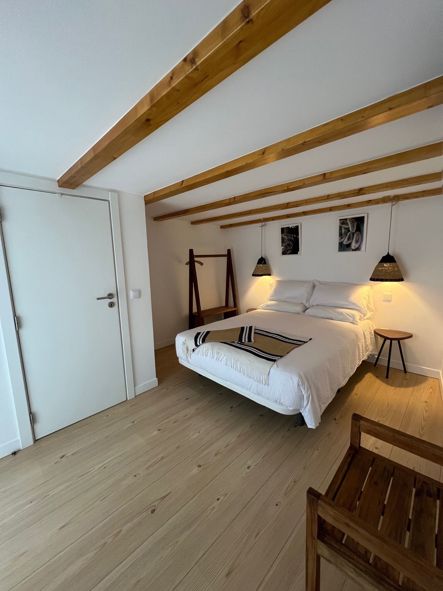 A bedroom with a bed, wooden beams, a door, and a small table.