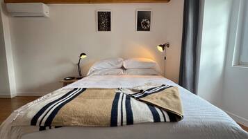 Une chambre à coucher comprenant un lit, deux lampes fixées au mur, une table de chevet, un climatiseur et deux tableaux encadrés accrochés au mur.