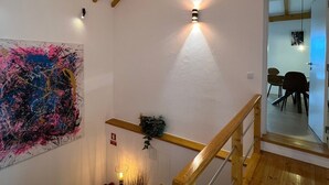 A staircase with wooden beams and a handrail, leading to a room with a painting and a wall-mounted light fixture. - Constância Guest House (Constância)