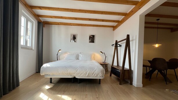 A bedroom with a large bed, wooden beams on the ceiling, a desk with a chair, and a dining area with chairs. - Constância Guest House (Constância)