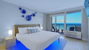 A hotel room with a large bed, a view of the ocean, and a balcony with chairs. - Villa Zafiro by Casanita - Oceanfront Suite (Myrtle Beach)