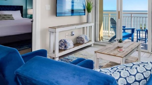 A modern room with a bed, a sofa, a coffee table, and a TV. There is a balcony with a view of the sea. - Villa Zafiro by Casanita - Oceanfront Suite (Myrtle Beach)