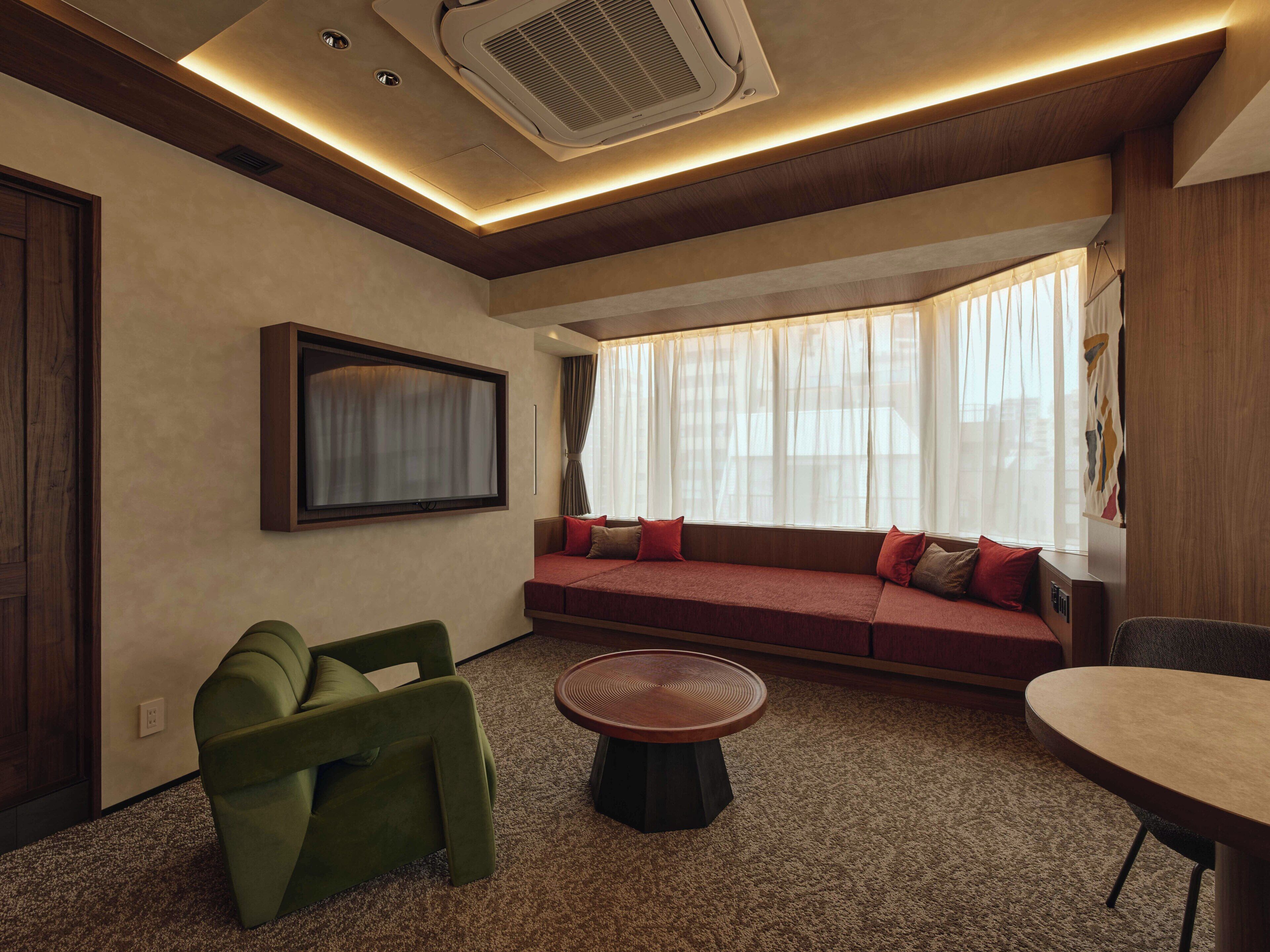 A modern room with a sofa, green armchair, round table, and a large window with curtains.
