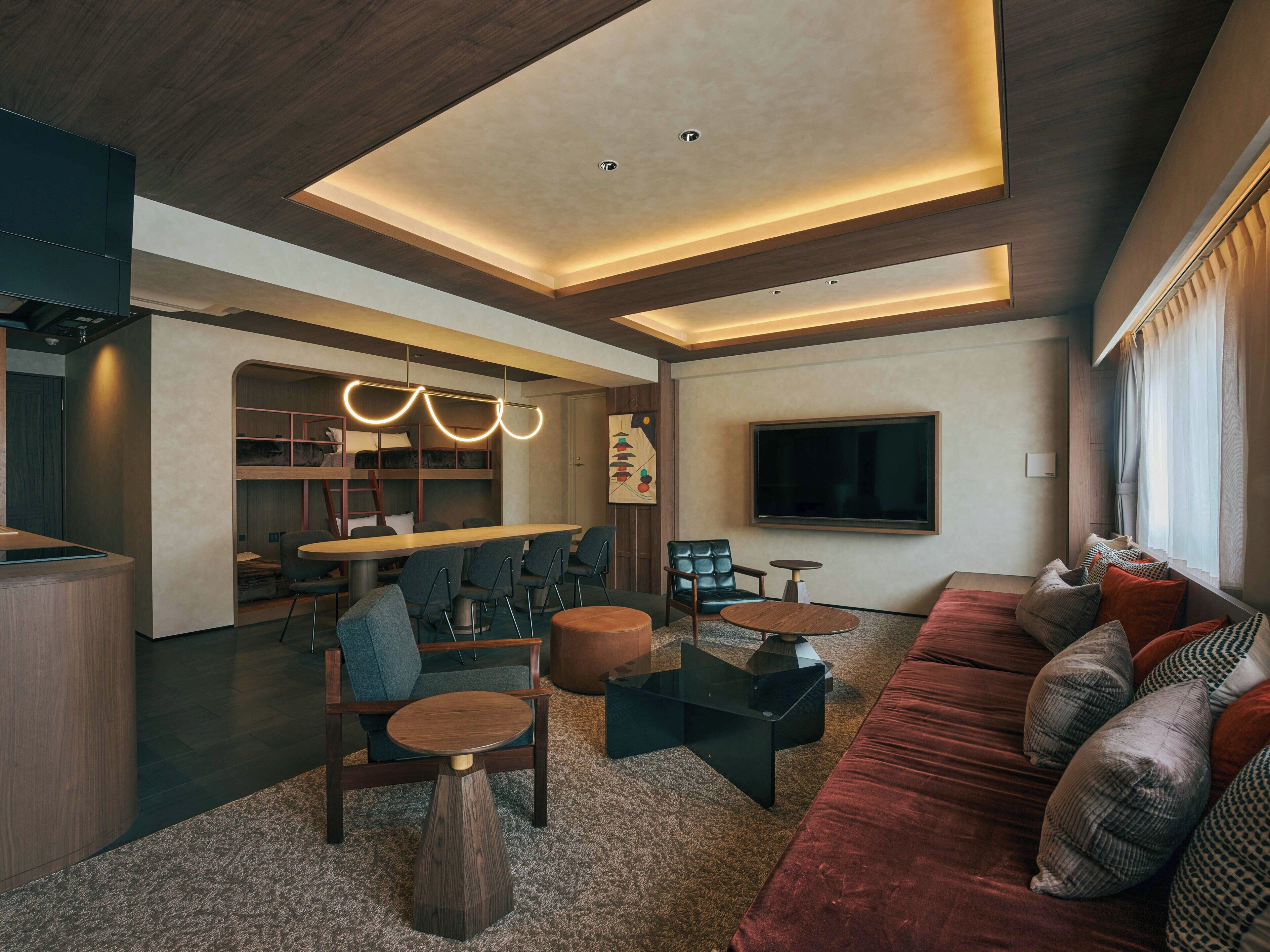 A modern living room with a sofa, chairs, a coffee table, a TV, and a built-in kitchen area.