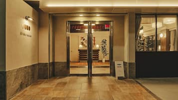 Een hotelentree met een receptiebalie, een potplant en een bord met de naam van het hotel.