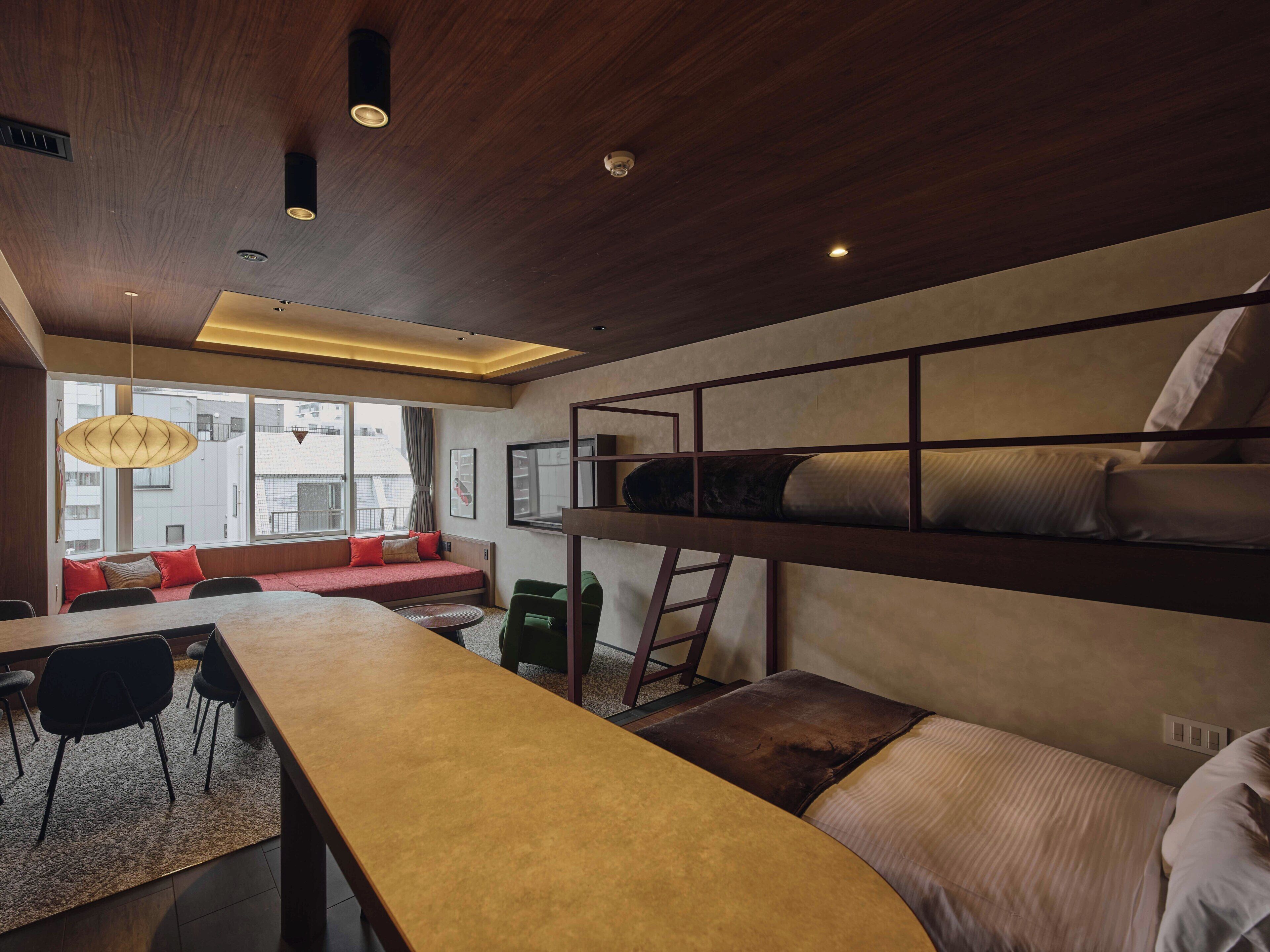 A modern room with a bunk bed, a dining table, chairs, a sofa, and a view of the city.