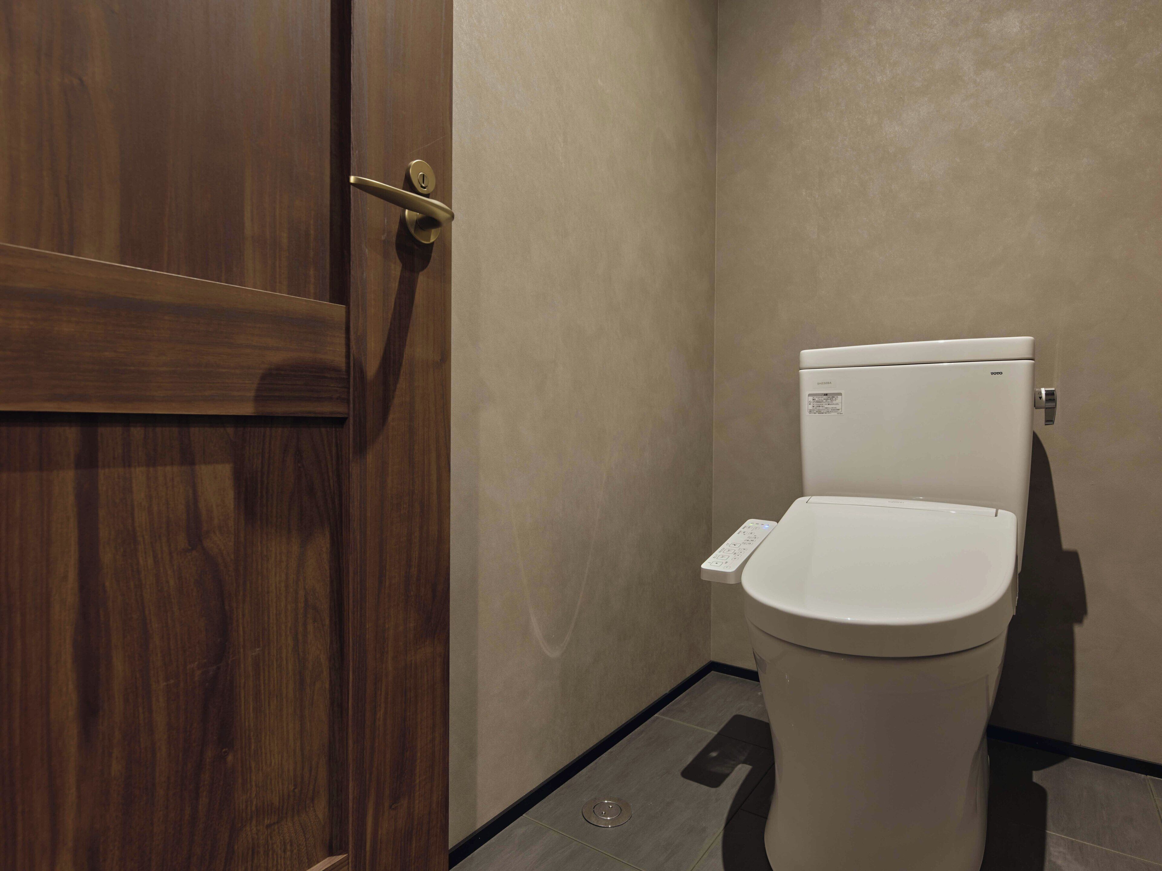 A bathroom with a wooden door, a white toilet, and a control panel.