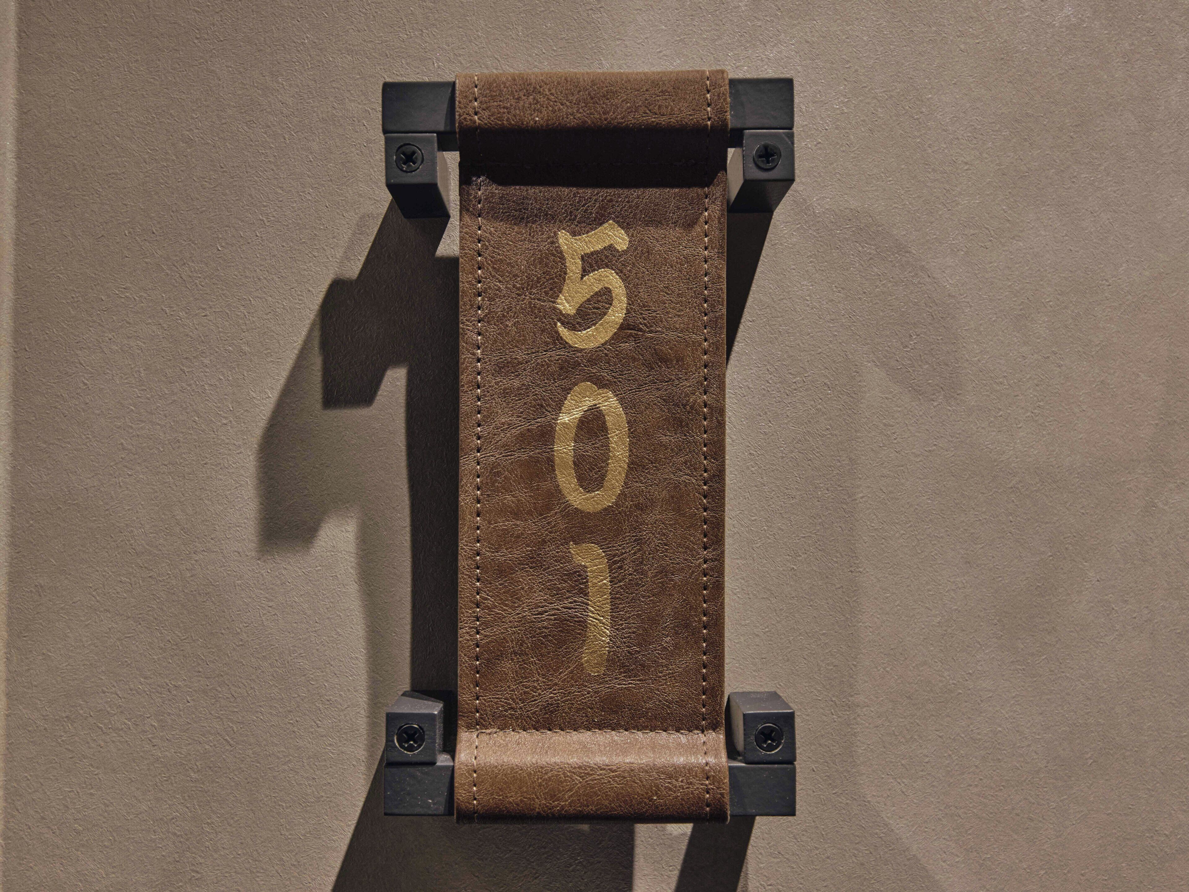 A brown leather strap with the number '501' embossed on it, mounted on a black metal frame against a textured wall.