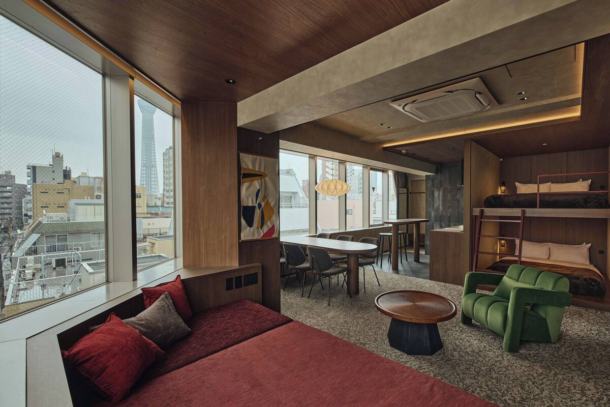 A modern hotel room with a large window, a sofa, a dining area, and a bunk bed.