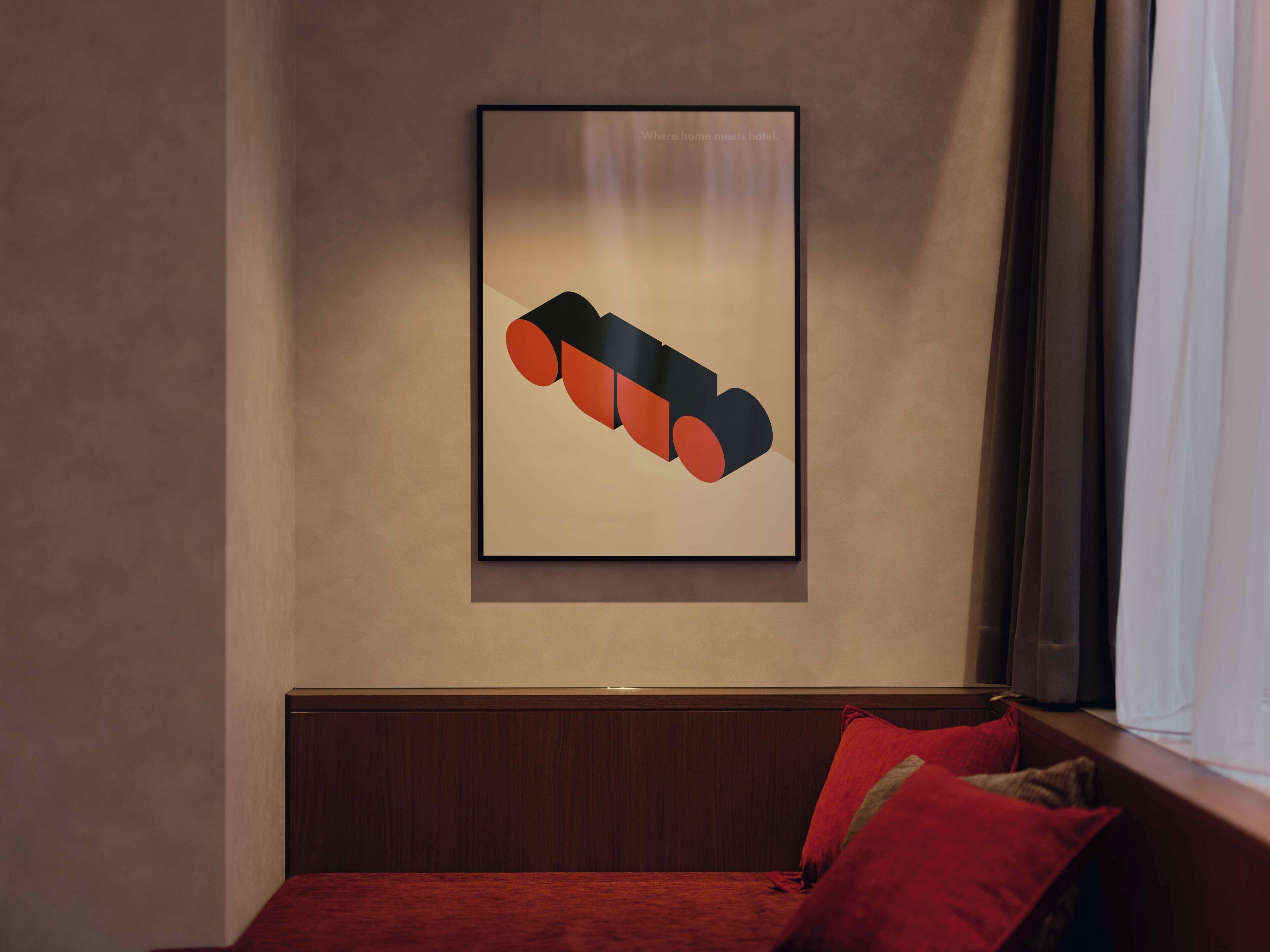 Ein gerahmtes abstraktes Kunstwerk an der Wand, eine hölzerne Bank mit roten Kissen und ein Fenster mit Vorhängen.