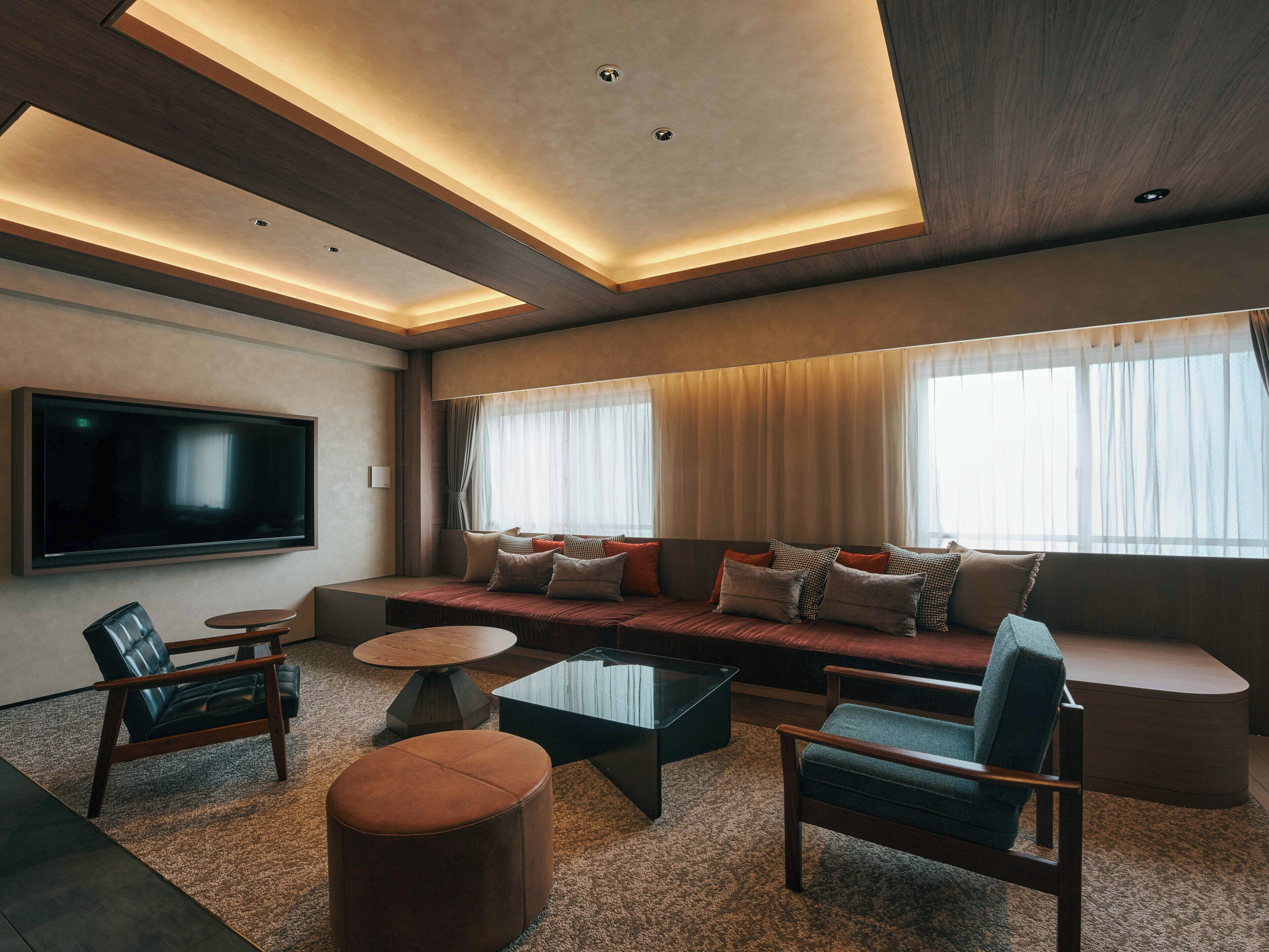 A modern living room with a large flat-screen TV, a sofa set, a coffee table, and seating arrangements.