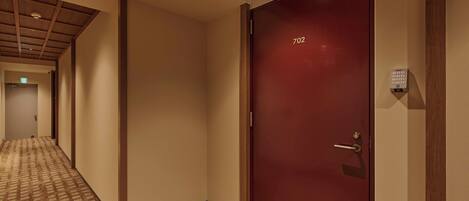 Un pasillo de hotel con alfombra estampada, techo de madera y una puerta roja con el número 702.