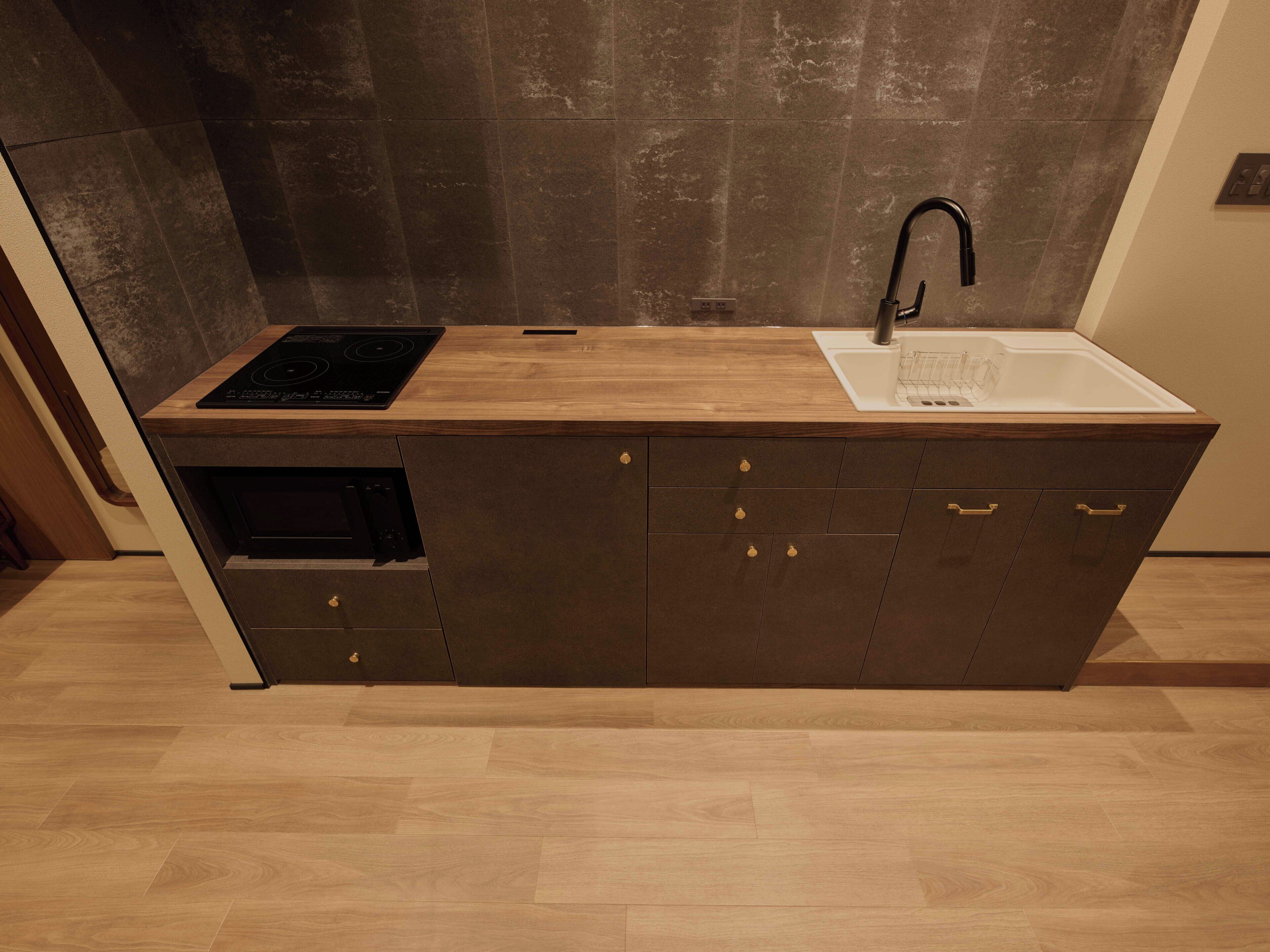 A modern kitchen with a wooden countertop, a built-in oven, a sink, and dark cabinets.