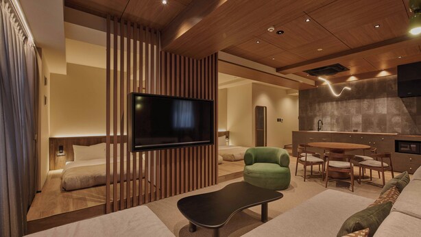 A modern hotel room with a flat-screen TV, a green armchair, a sofa, and a dining area with a table and chairs. - illi Aest Shinagawa-Gotanda (Tokyo)
