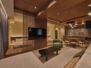 A modern hotel room with a flat-screen TV, a green armchair, a sofa, and a dining area with a table and chairs. - illi Aest Shinagawa-Gotanda (Tokyo)