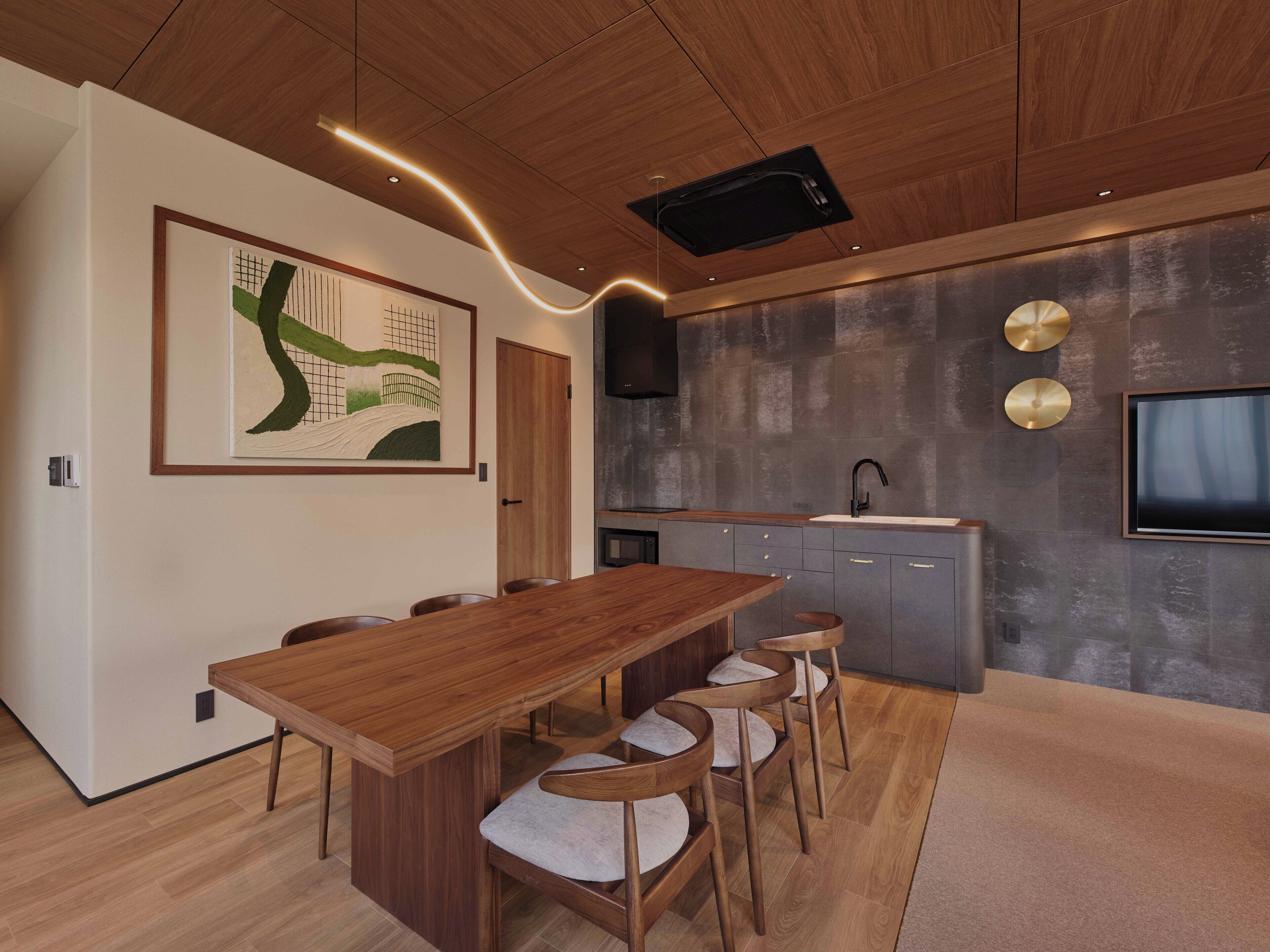 Eine moderne Küche mit Holztisch und -stühlen, einem Einbauofen und einem großen Fernseher an der Wand.