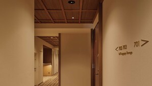 A hotel hallway with a patterned carpet, wooden ceiling beams, and directional signs indicating room numbers. - illi Aest Shinagawa-Gotanda (Tokyo)