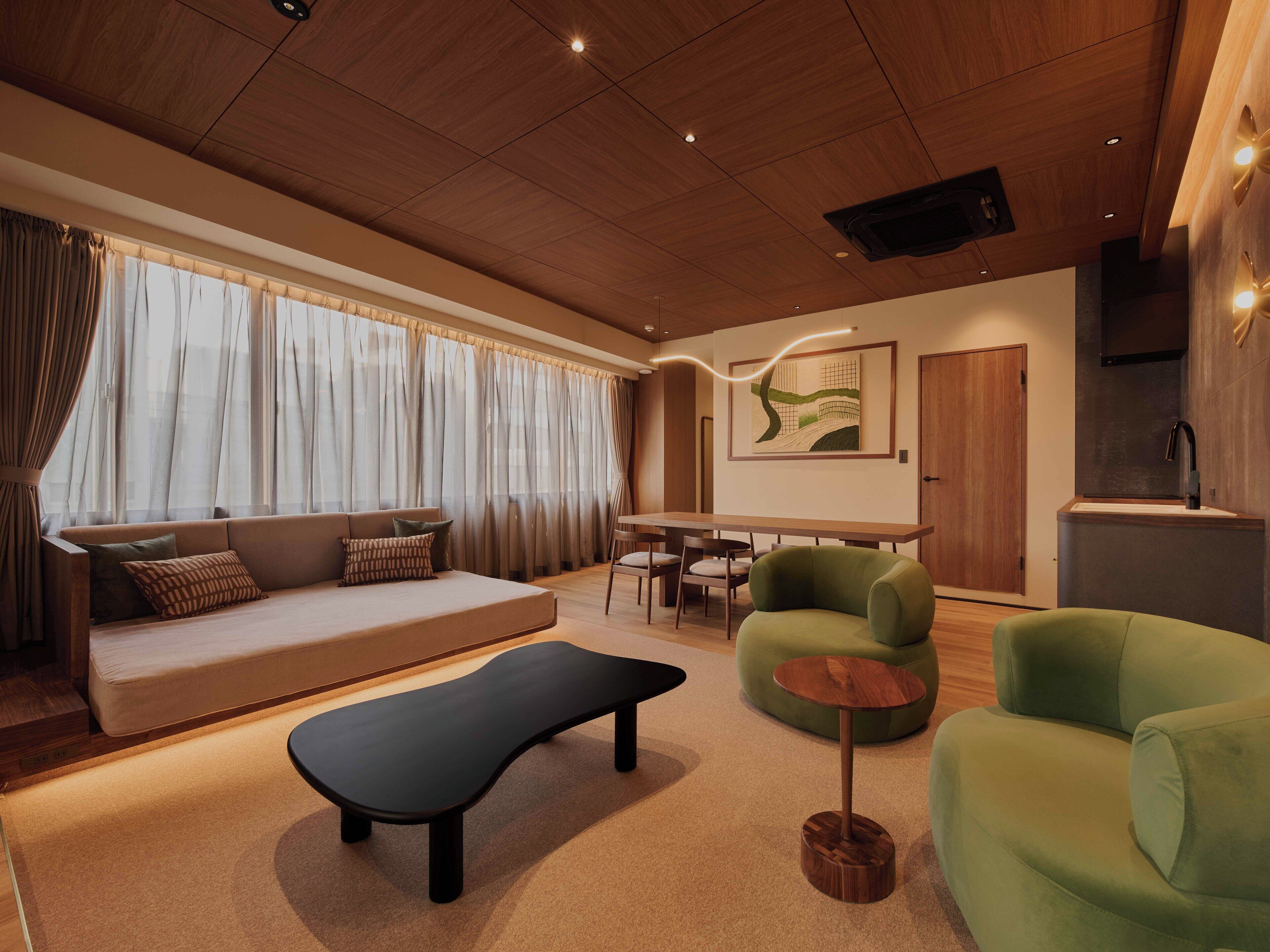 A modern living room with a sofa, green armchairs, a black bench, and a dining area.