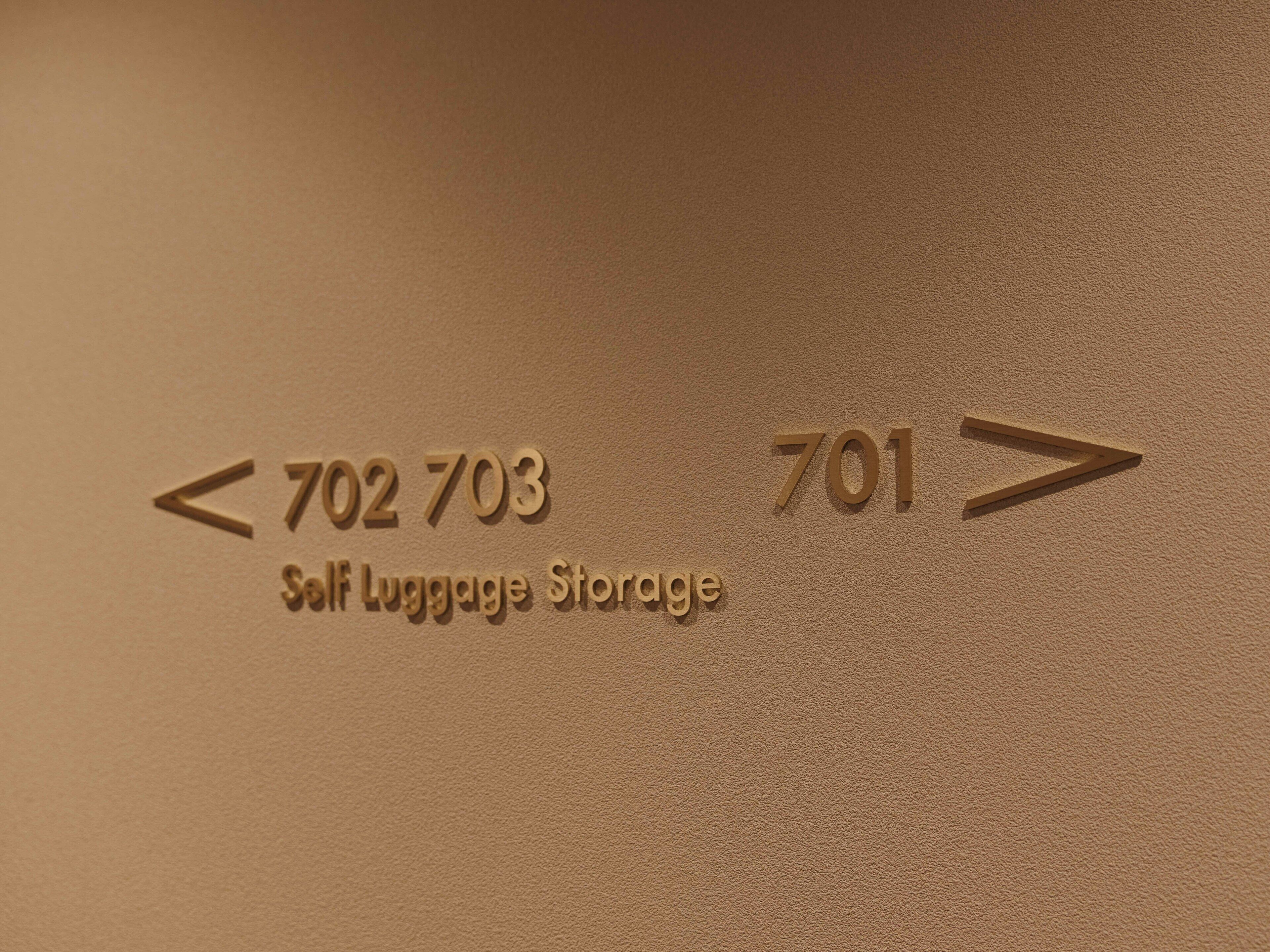 Bord dat zelfbagageopslag aangeeft, met richting pijlen en nummers <702 703 en 701>.