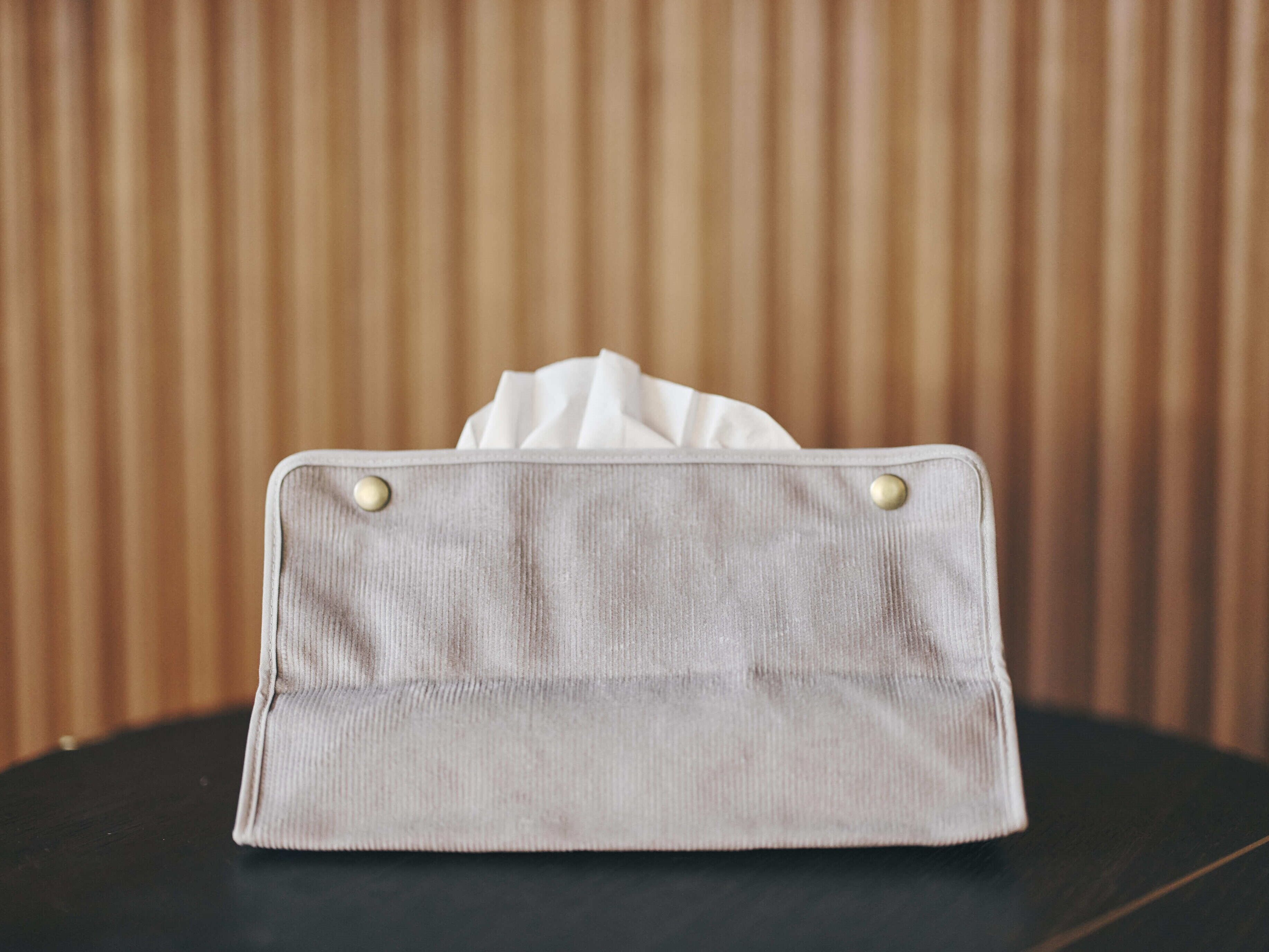 Un sac en tissu gris clair orné de deux boutons dorés, posé sur une surface sombre, avec un fond en bois.