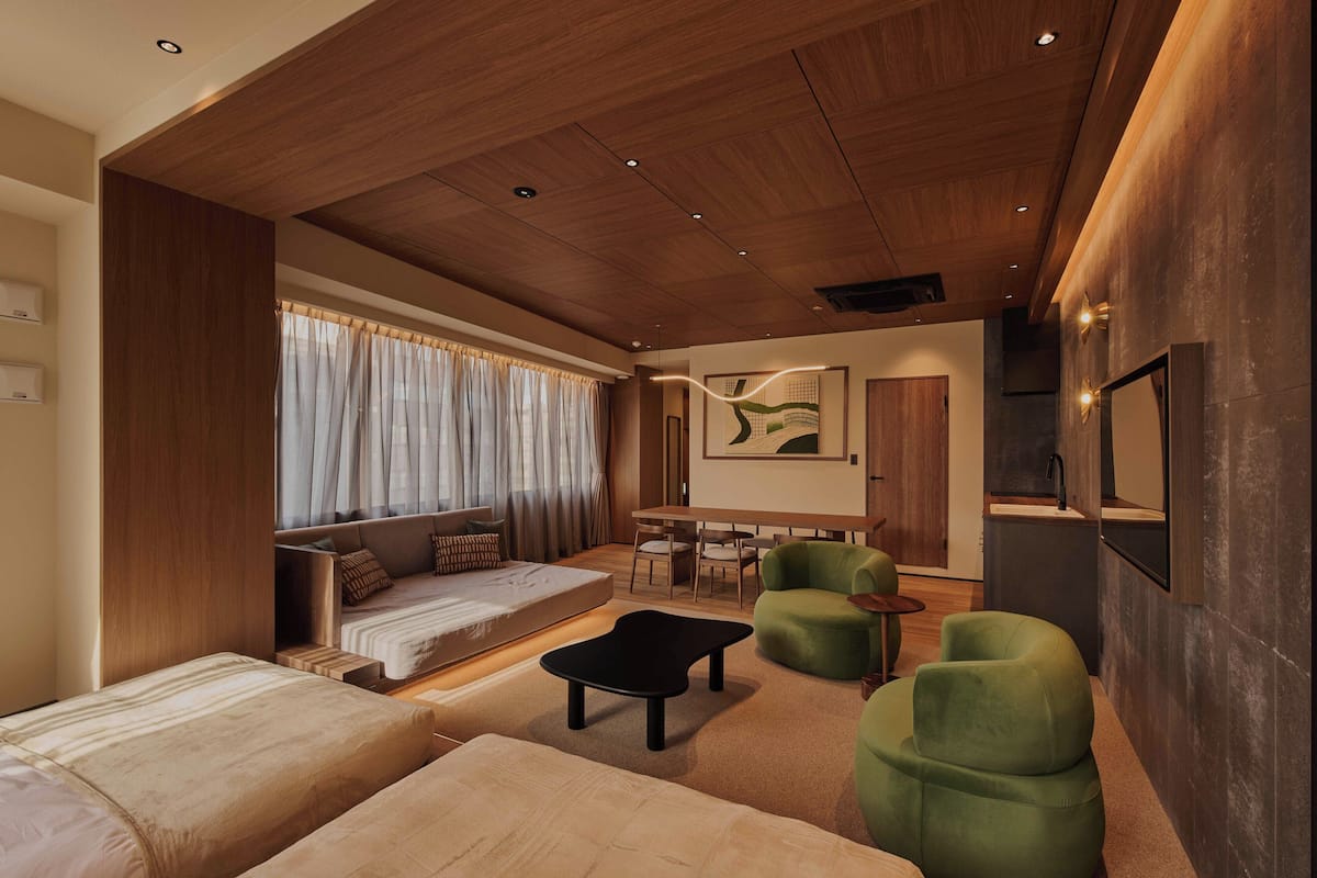 A modern living room with a sofa, green armchairs, a coffee table, and a dining area with a table and chairs.
