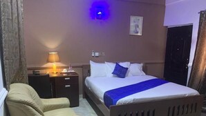 Et hotelværelse med seng, natbord, lampe og stol.