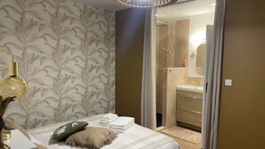 Un dormitorio con cama, mesita de noche, lámpara y baño visible a través de una puerta corredera.