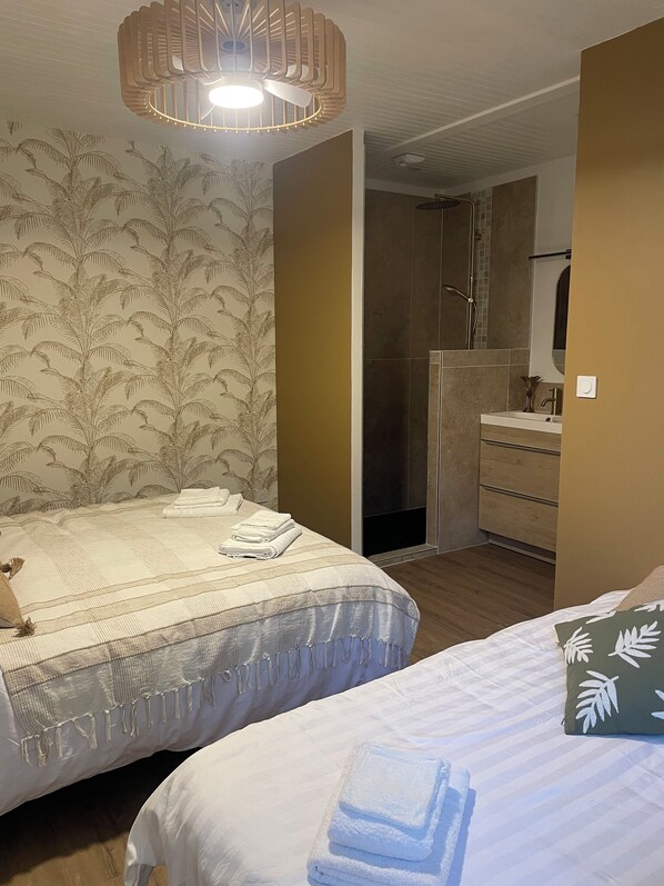 A hotel room with two beds, a bathroom with a shower, and a wooden floor.