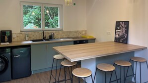 Una cocina moderna con una isla grande, taburetes de bar, lavadora y ventana con vista a zonas verdes.