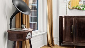 A vintage gramophone on a wooden stand, a window with curtains, and a dark wooden cabinet with a mirror. - Gatsby-inspired mansion w/ game lounge & hot tub! (Louisville)