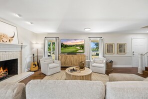 A living room with a fireplace, a television, and a view of a golf course.