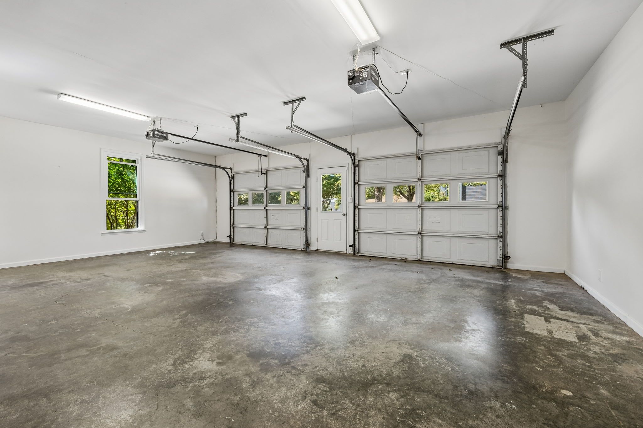 Een garage met witte wanden, een betonnen vloer en een groot raam aan de linkerkant.