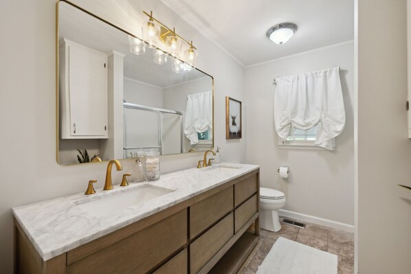A bathroom with a double sink vanity, a large mirror, and a toilet.
