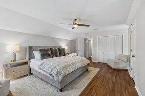A bedroom with a bed, bedside tables, a nightstand, a ceiling fan, a wardrobe, and a chair.