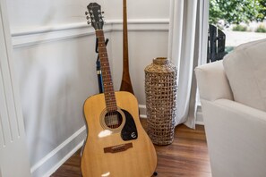 Una guitarra apoyada en una pared, una cesta tejida y un sofá blanco en una habitación con suelo de madera.