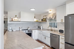 A modern kitchen with white cabinetry, a marble countertop, and stainless steel appliances.