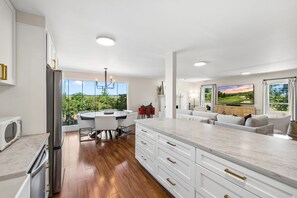 A modern kitchen with a large island, wooden flooring, and a dining area with a view.