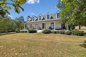 A two-story house with a covered porch, a small front yard, and a tree to the right.