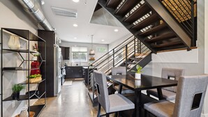 A modern kitchen with dark cabinetry, a central island, and a staircase with a wooden finish. - Cozy 3-Story Townhome w/ Rooftop & Skyline Views! (Nashville)