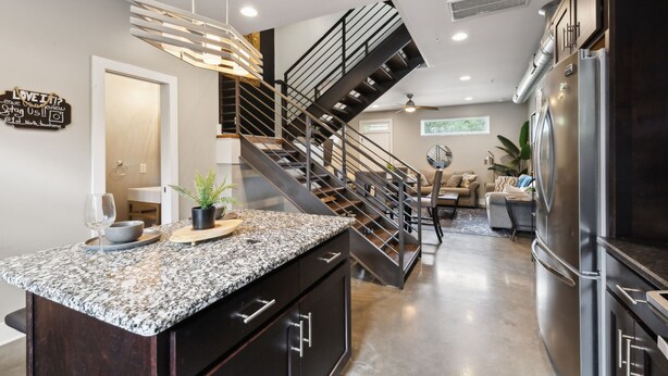 A modern kitchen with a granite countertop, stainless steel appliances, and a black staircase. - Cozy 3-Story Townhome w/ Rooftop & Skyline Views! (Nashville)