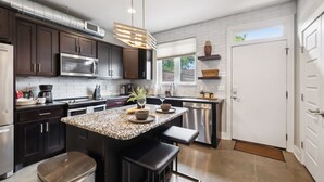 A modern kitchen with dark wood cabinets, stainless steel appliances, a granite countertop, and a built-in island with seating. - Cozy 3-Story Townhome w/ Rooftop & Skyline Views! (Nashville)