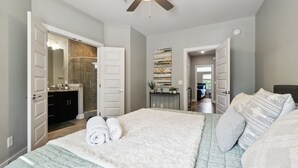 A bedroom with a large bed, a ceiling fan, and a view into the bathroom. - Cozy 3-Story Townhome w/ Rooftop & Skyline Views! (Nashville)